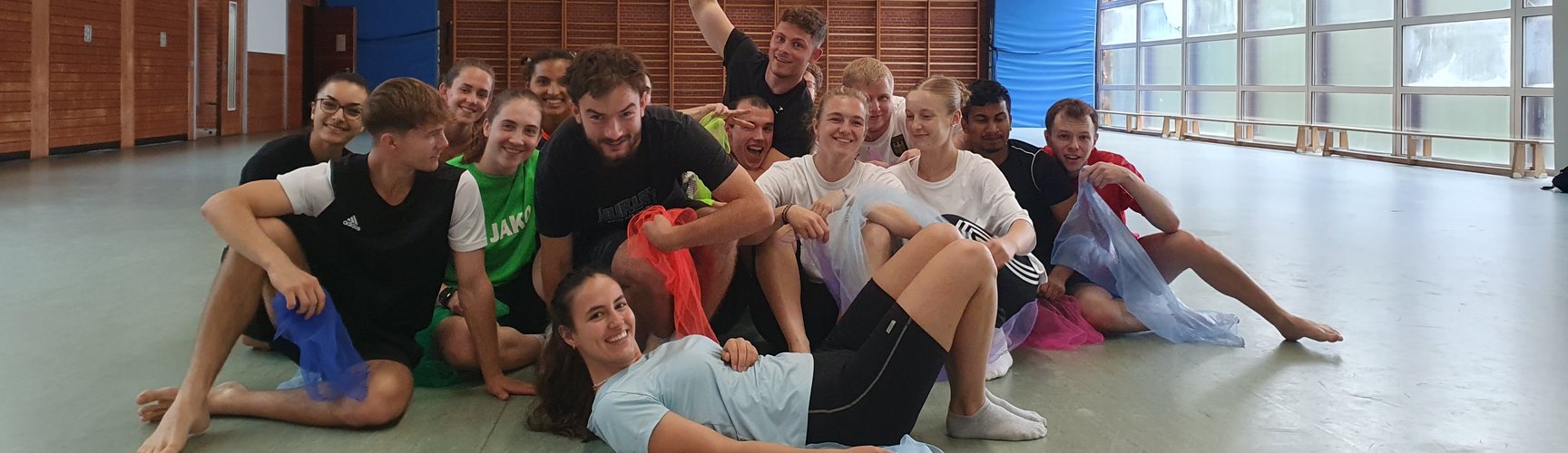 Eine Gruppe Studierender posiert fröhlich in einer Sporthalle