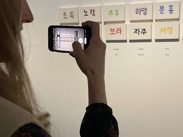 Jemand fotografiert kleine Schilder mit Schriftzeichen, die an der Wand hängen.