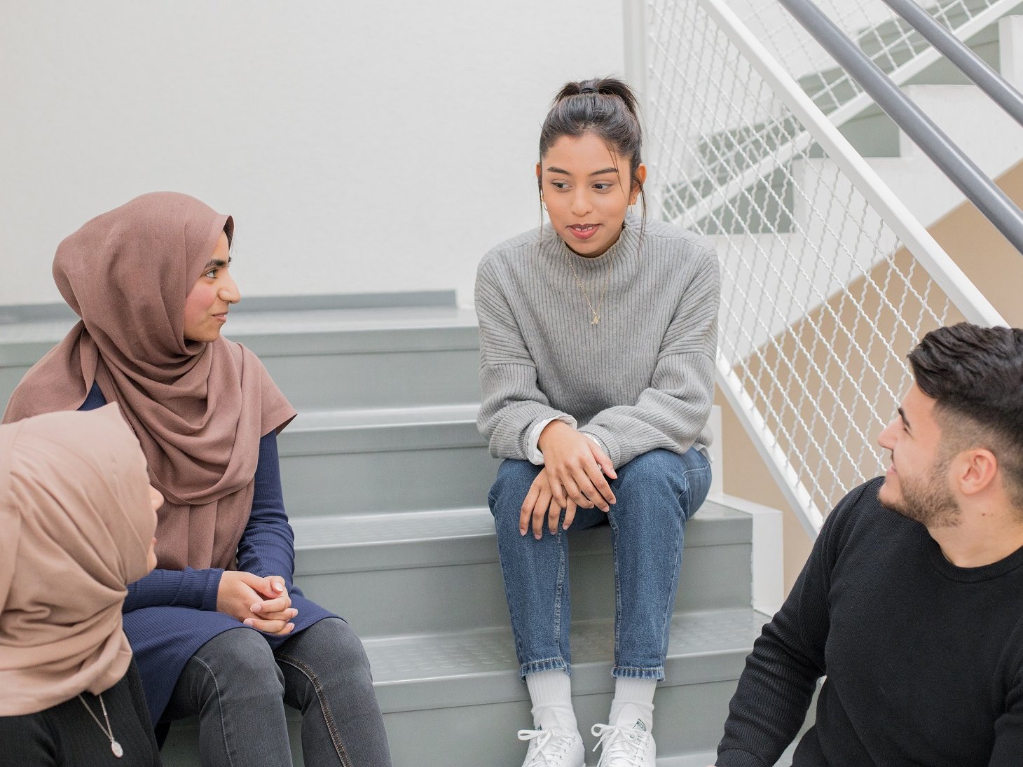 Drei Studentinnen und ein Student sitzen auf einer Treppe und unterhalten sich.