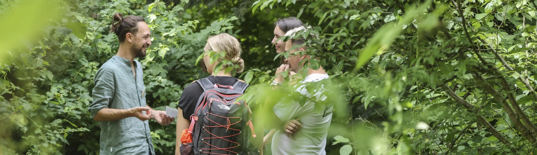 Ein Dozent steht mir drei interessierten Personen in einem Landschaftsgarten