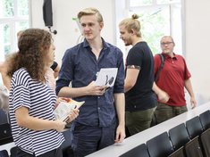 Zwei Studierende unterhalten sich, im Hintergrund stehen weitere Studierende.