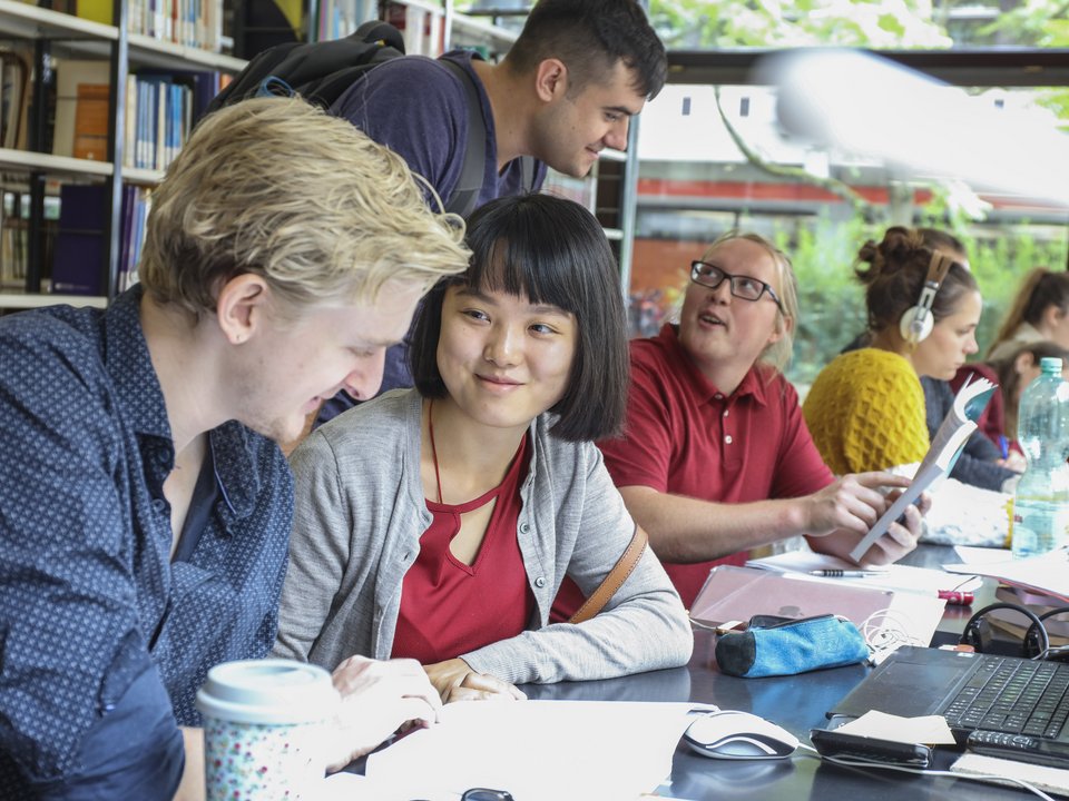 Studierende lernen im ruhigen Bereich der Bibliothek der PH Karlsruhe. Hinter ihnen, sind Bücherregale zu sehen. Sie befinden sich im Gebäude 2.