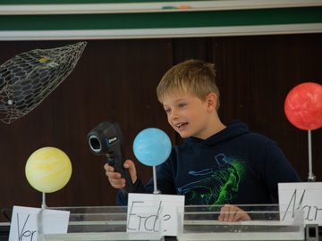 Junge hält ein Infrarotthermometer auf ein Modell der Venus.