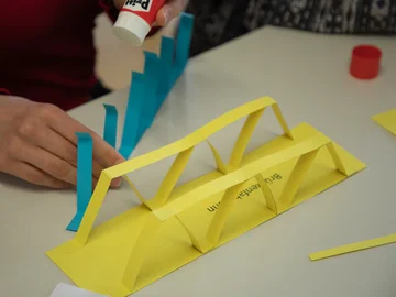 Jemand bastelt eine Brücke aus gelbem und blauem Tonpapier.