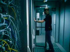Ein Mann steht in einem Serverraum vor einem Schrank mit vielen Kabeln
