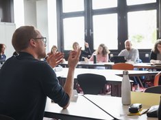 Szene aus einer Weiterbildungsveranstaltung: Personen sitzen in einer Runde und diskutieren, ein Mann im Vordergrund spricht gerade