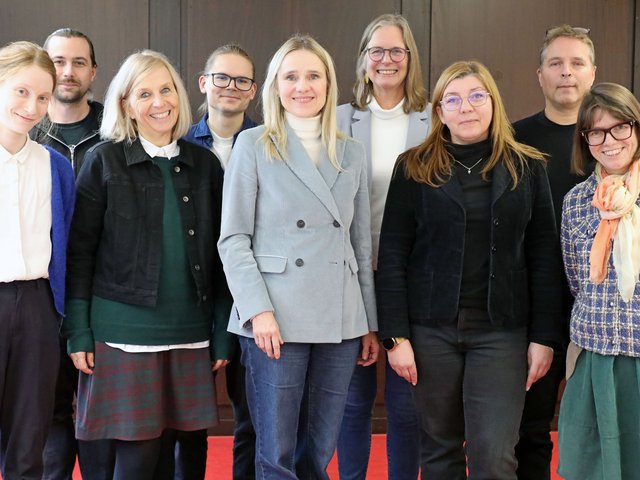 Gruppenfoto von neun Personen verschiedenen Alters und Geschlechts.