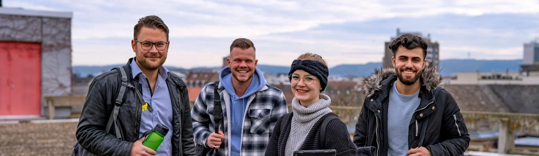 Vier Studierende stehen auf dem Dach der Hochschule und lachen in die Kamera