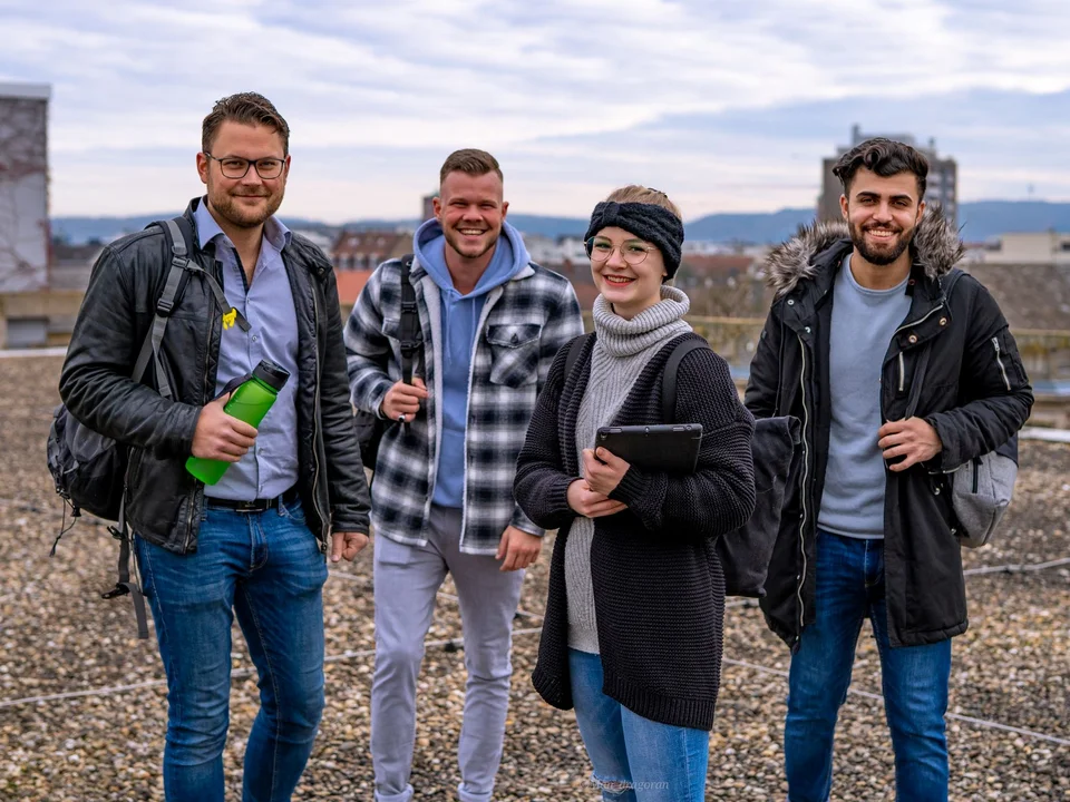 Vier Studierende stehen auf dem Dach der Hochschule und lachen in die Kamera