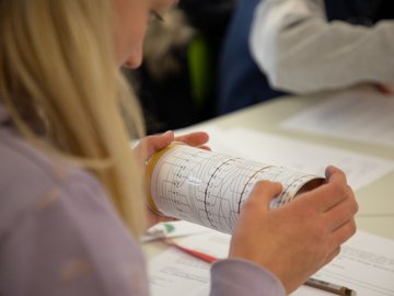 Eine Schülerin ist von hinten am Tisch zu sehen, in der Hand hat sie eine Rolle mit Daten eingestanzt.