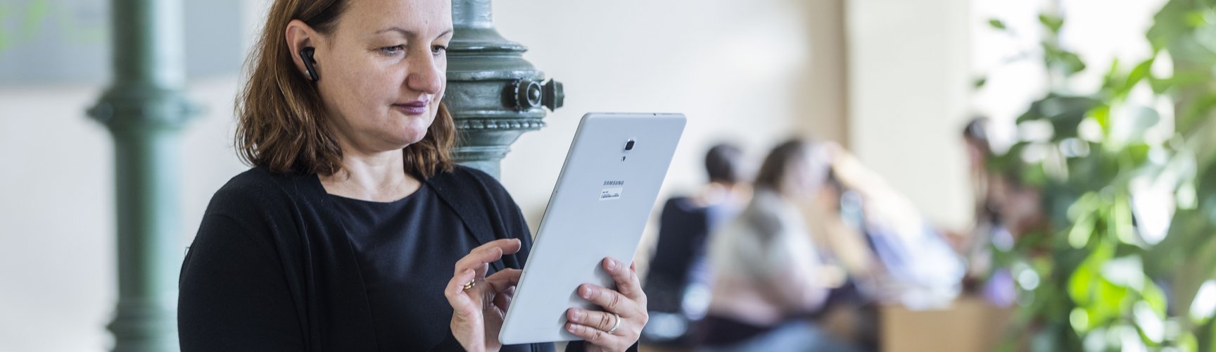 EIne Frau mittleren Alters steht in einem Flur und bedient ein Tablet