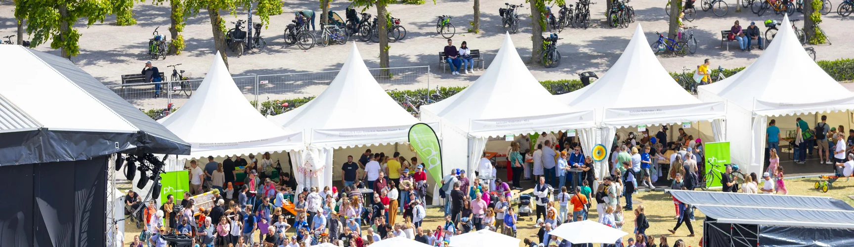 Ein Blick von oben auf das EFFEKTE Wissenschaftsfestival 2025. Zu sehen sind die von der PHKA bespielten Pagodenzelte, ein teil von der bühne und sehr viele Menschen. 