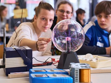 Drei Schüler:innen experimentieren an einer Plasmalampe.