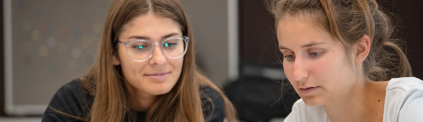 Zwei Studentinnen in einem Seminarraum blicken gemeinsam auf ein Tablet.