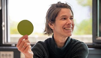 Key Visual MA Erwachsenenbildung Eine Person hält einen grünen Punkt aus Papier in die Höhe.