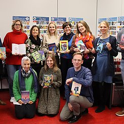 Eine Gruppe Menschen mit Büchern in den Armen und Bücherplakaten im Hintergrund.