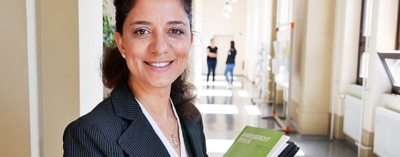 Eine Person blickt in die Kamera. Sie trägt Mappen im Arm.